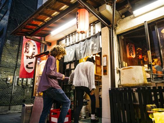 Hipster young man and woman walking into Japanese bar with lanterns, nightlife, date, food and drink
