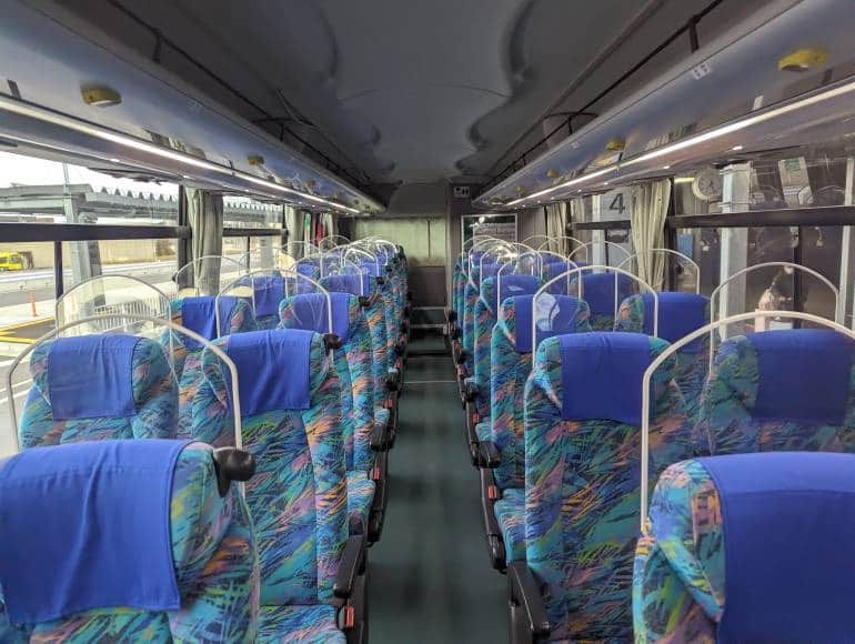 The inside of a bus with empty pairs of seats on both sides.